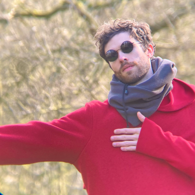 a man in a red sweater, grey scarf and circular black sunglasses extends his right arm
